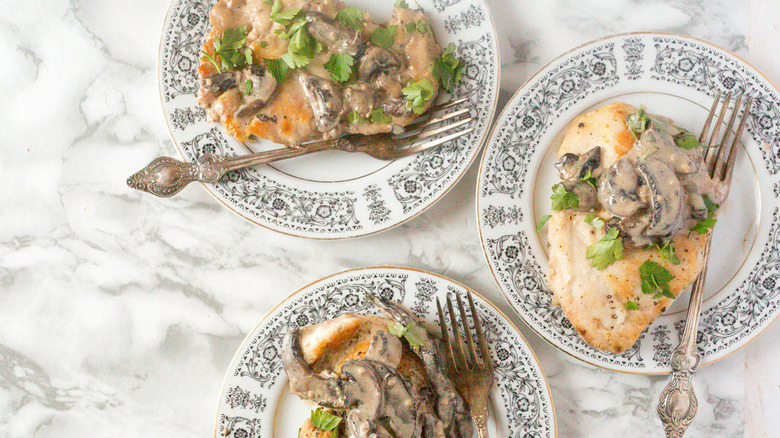 Three servings of chicken marsala plated and topped with herbs