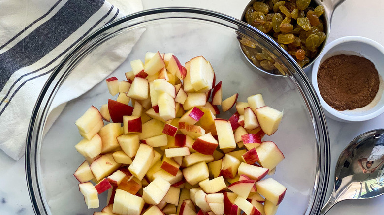 apples in bowl surrounded by bowls of raisins and cinnamon