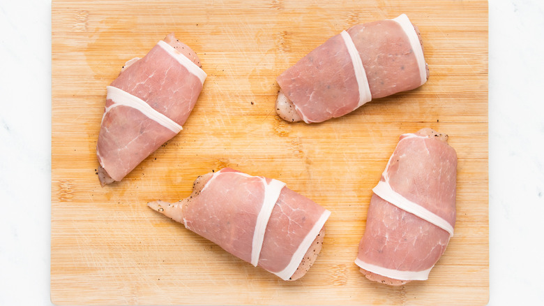 Chicken wrapped in bacon on chopping board