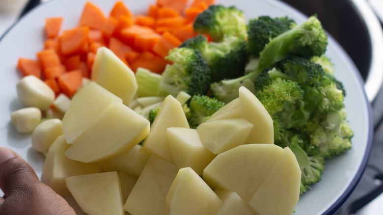 plate of chopped potatoes, broccoli, garlic cloves, celery, and carrots