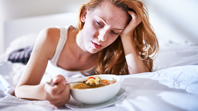 A woman eating soup in bed