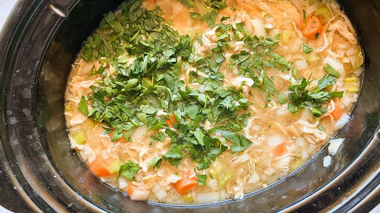 A slow cooker with soup topped by fresh parsley