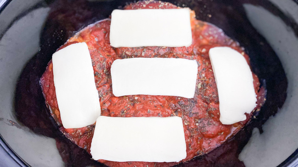 mozzarella cheese slices sitting on top of pasta sauce covering chicken breasts in slow cooker