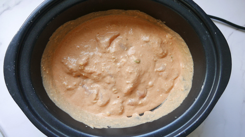 pureed sauce ingredients poured over chicken in slow cooker