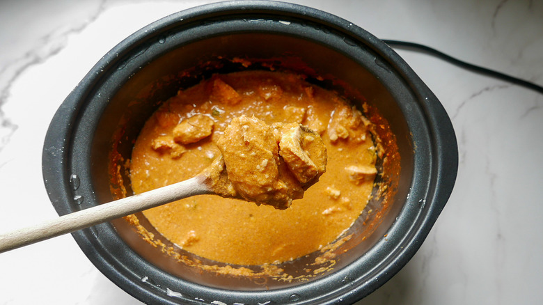 wooden spoonful of creamy coconut chicken curry with cashews in a slow cooker