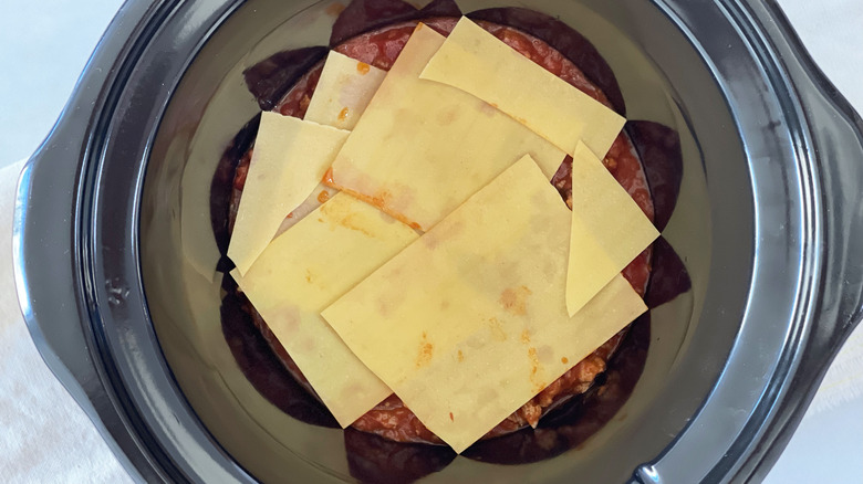 slow cooker pot with sauce and lasagna noodles