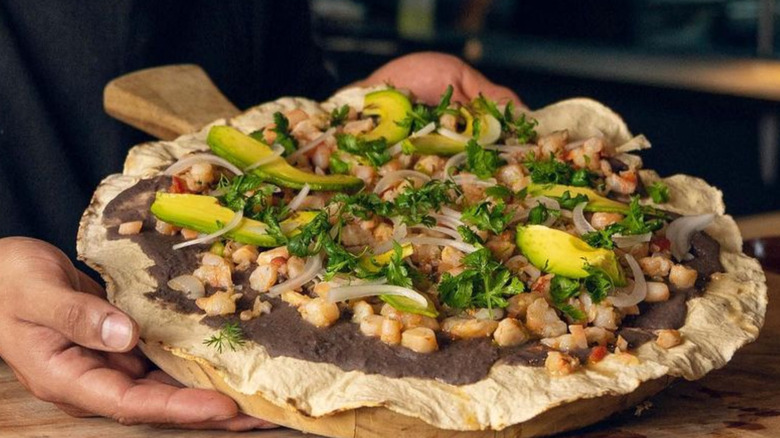 Large, thin corn tortilla with bean paste, onions, and avocado.