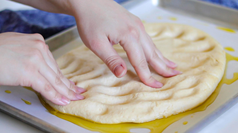 hands patting down pizza dough