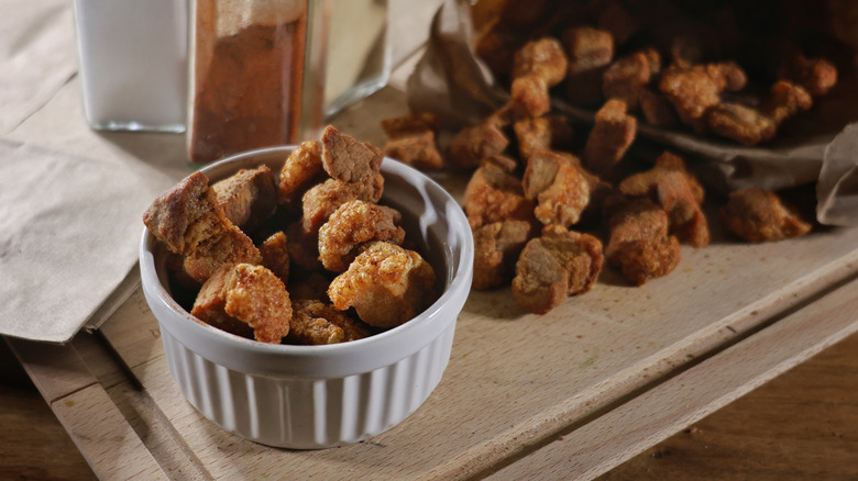 Ramekin of pork cracklins with more spilling onto cutting board