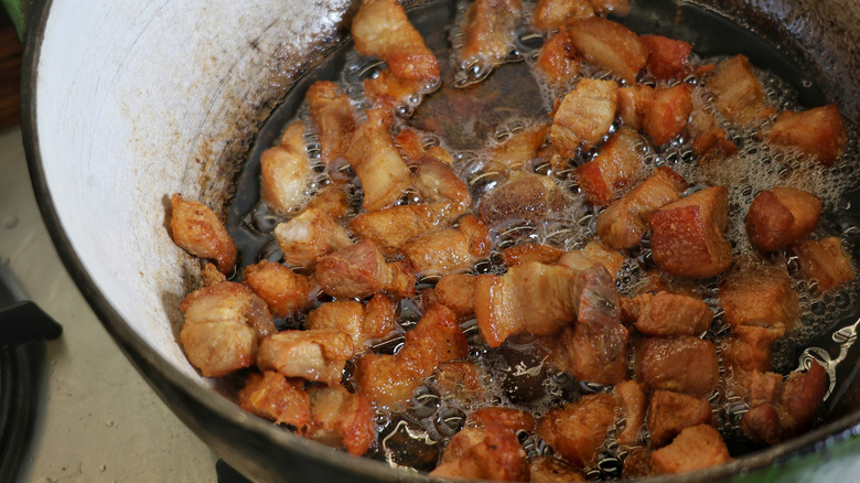 Dutch oven full of frying pork belly pieces