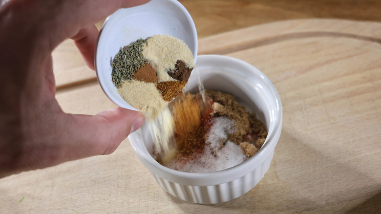 Hand pouring seasonings into a ramekin