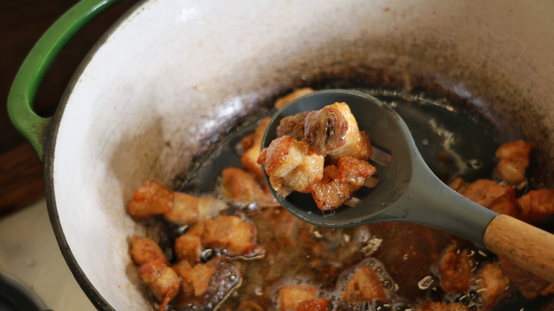 Slotted spoon scooping pork belly pieces out of Dutch oven