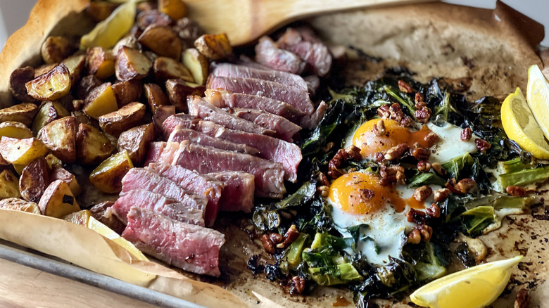 Sheet pan with potatoes, steak slices, eggs, collard greens, and lemon slices