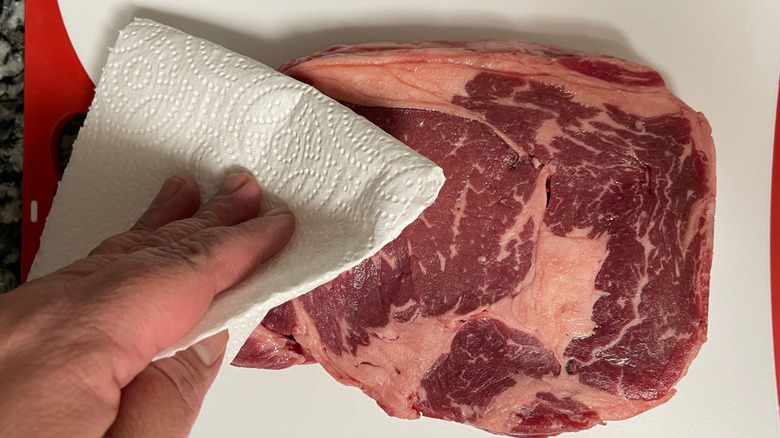 Hand patting raw steak with paper towel