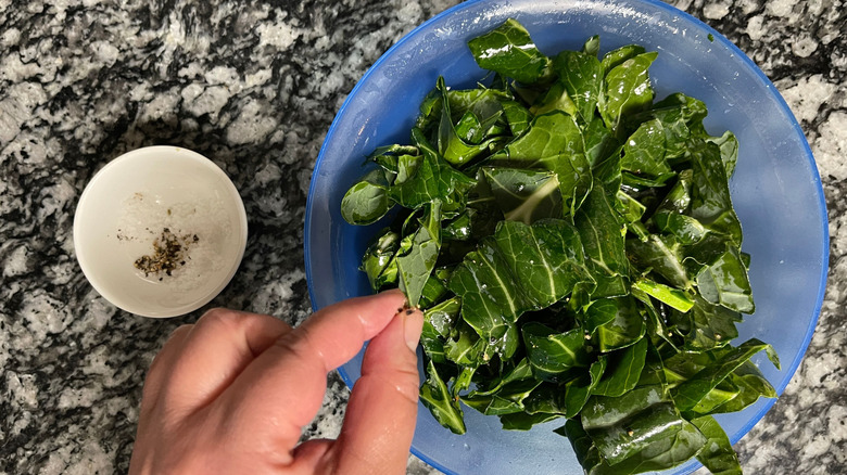 Hand sprinkling salt and pepper onto collard greens