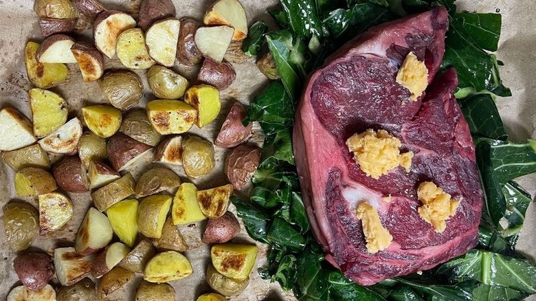 Potatoes, collard greens, and steak with butter on sheet pan