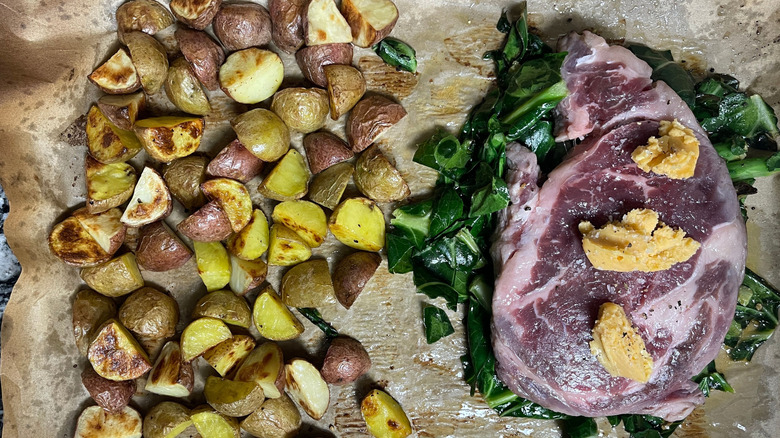 Potatoes, collard greens, and steak with butter on sheet pan