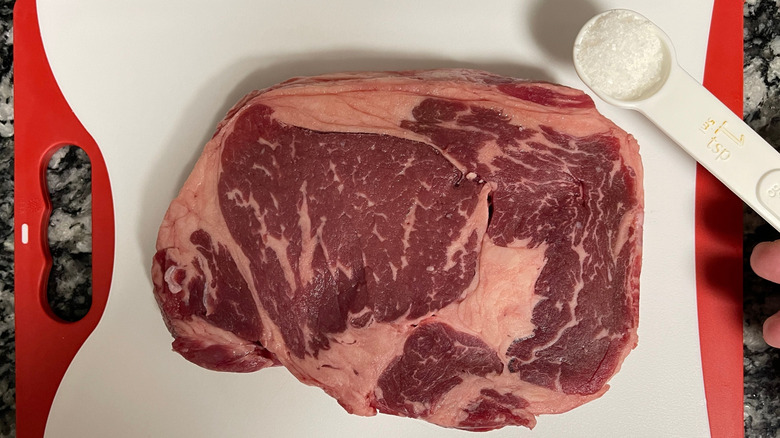 Raw steak on cutting board next to teaspoon of salt