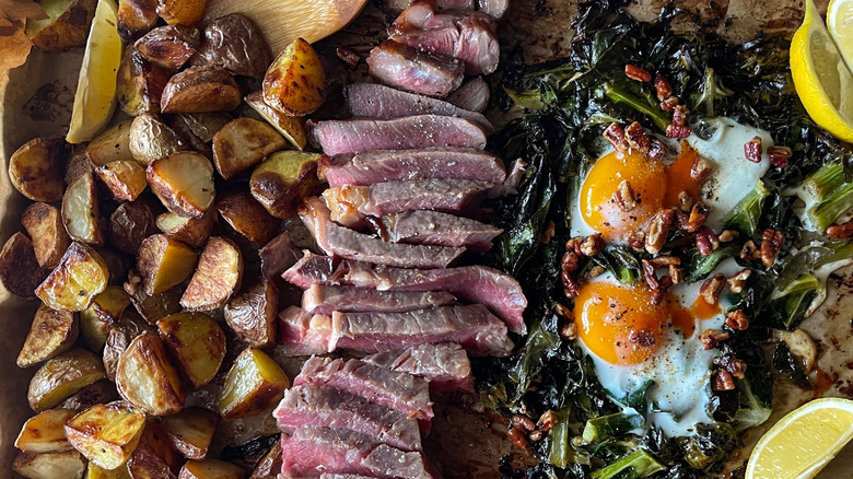 Potatoes, sliced steak, collard greens, eggs, pecans, and lemon wedges on sheetpan