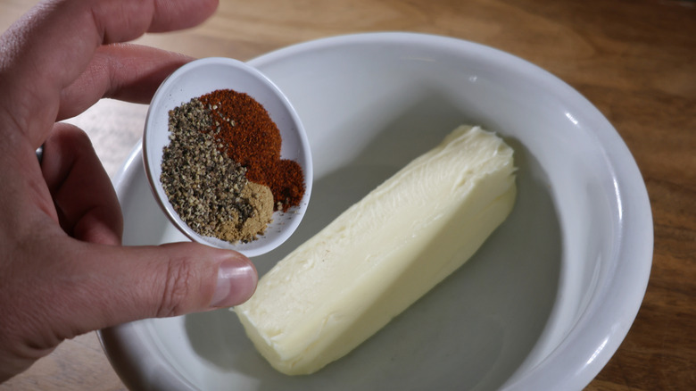 Pouring a small dish of spices onto stick of butter in a bowl