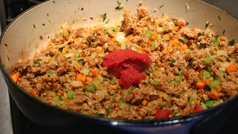 tomato paste atop meat and vegetables in skillet