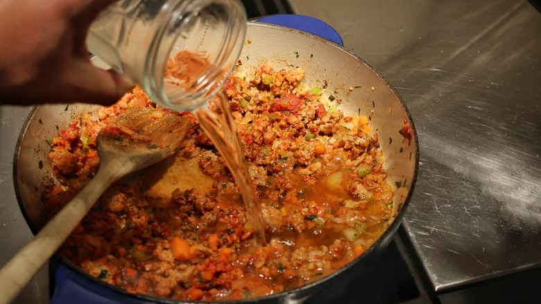 pouring white wine into skillet of ragu