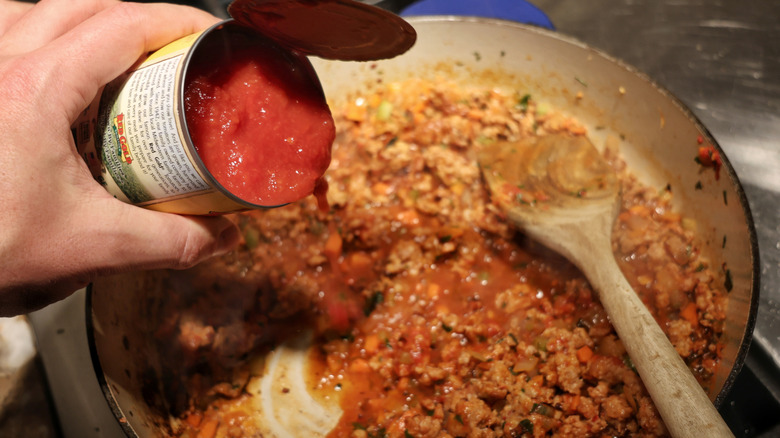 open can of tomatoes above skillet of ragu