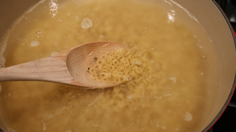 wooden spoon holding uncooked pasta in pot of water