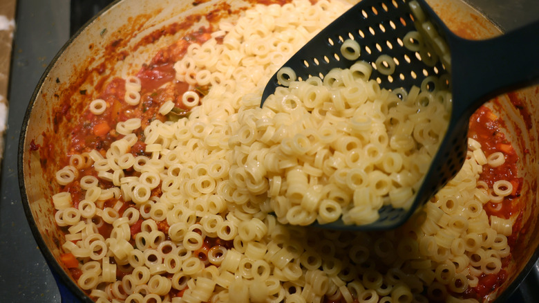 scooping cooked pasta into pot of ragu