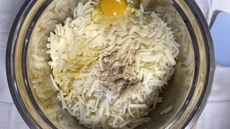 hash browns in bowl with egg, seasonings, and butter