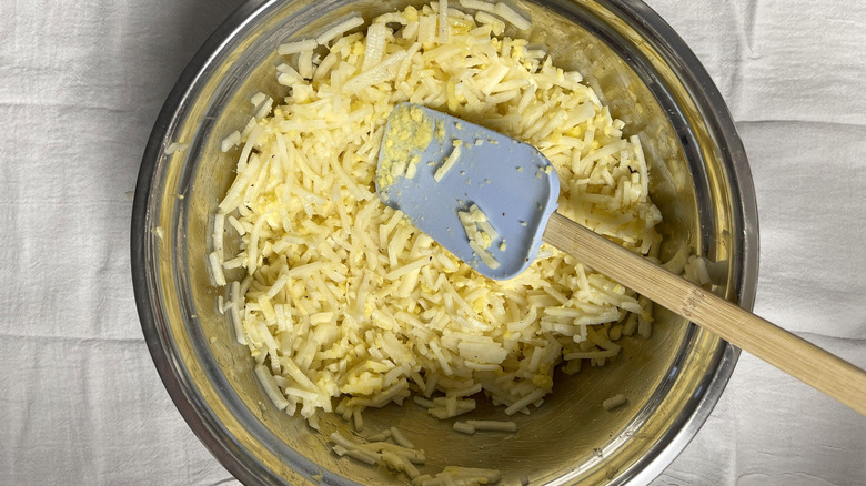 hash browns in bowl mixed with egg, seasonings, and butter