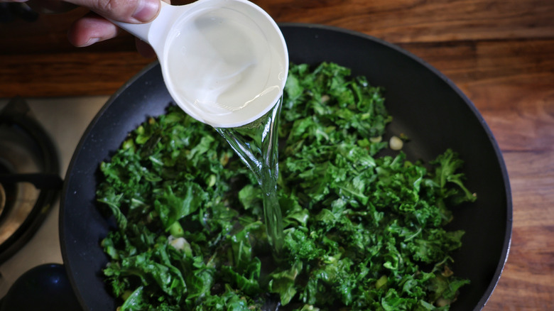 pouring water into skillet of kale