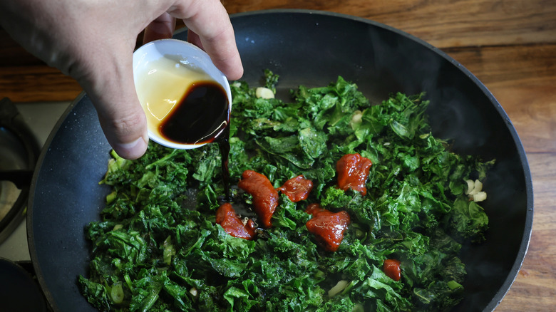 pouring soy sauce into skillet of kale