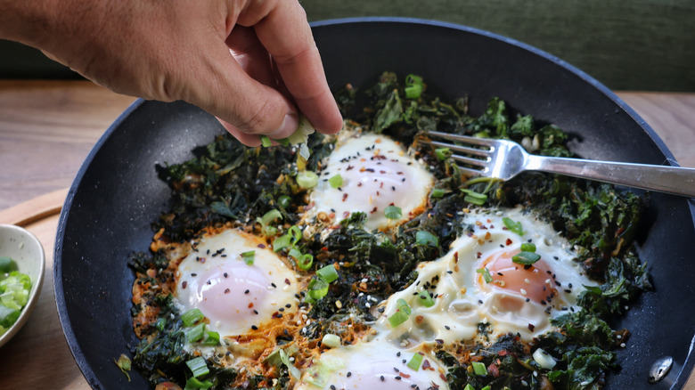 sprinkling scallions into skillet of eggs and kale