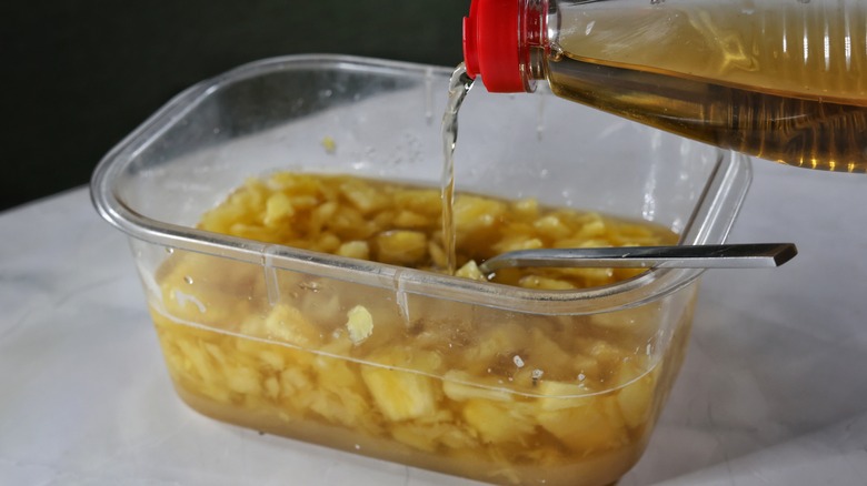 pouring cider vinegar into container of pineapple