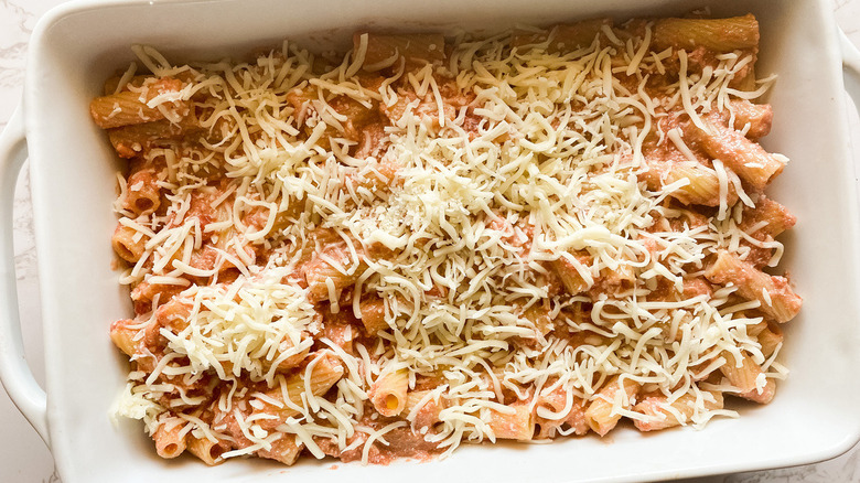 Pasta mixture with shredded cheese in a baking dish