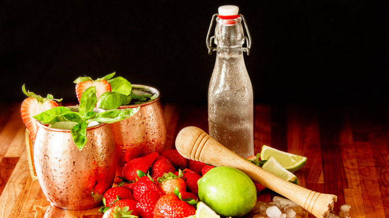 Strawberry Moscow mules surrounded by fresh fruit and bottle of simple syrup
