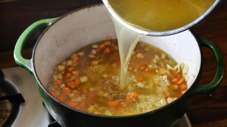 pouring broth into pot of vegetables