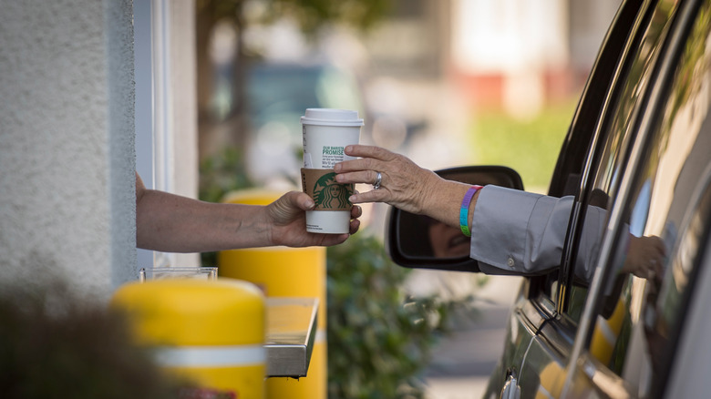 Worker handing Starbucks drink at drive-thru window