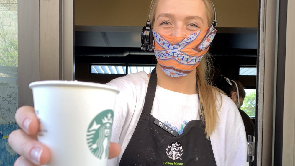 starbucks employee with mask serving drink at drive thru