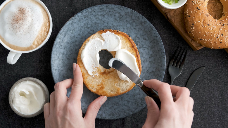 woman spreading cream cheese on bagel