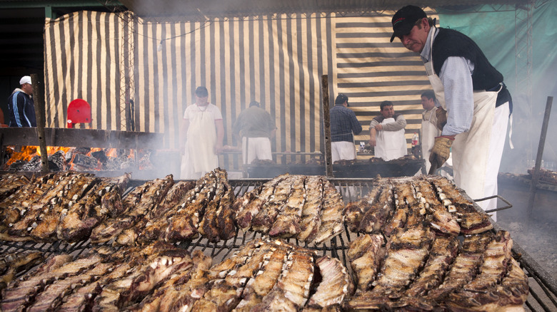 man attends argentinian asado steaks on grill