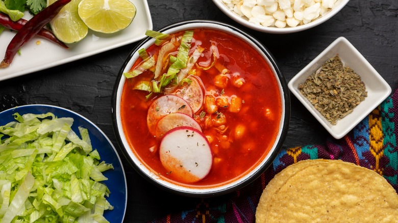 Pozole roja with sides of lettuce, lime wedges, and tortillas