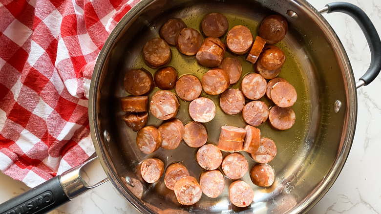 andouille sausage slices cooking in a skillet