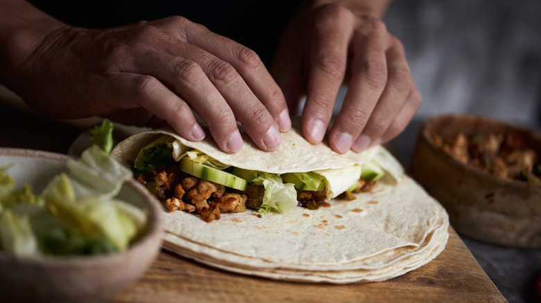 Hands rolling burrito on cutting board