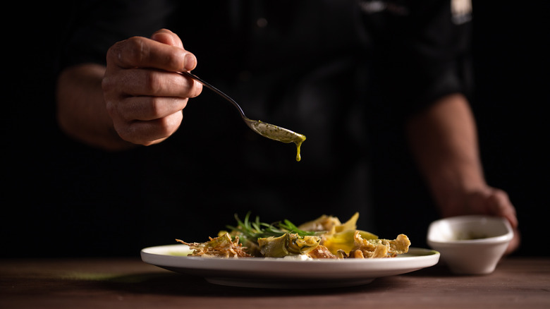 Chef spooning condiment onto plate