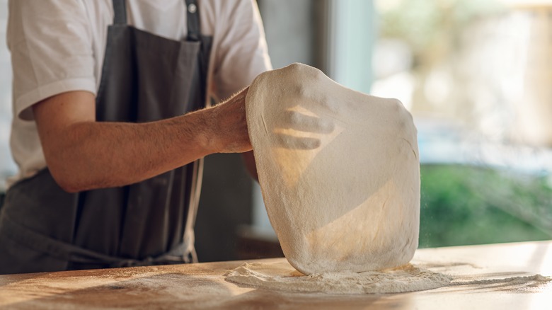 person stretching pizza dough