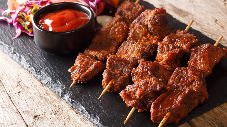 Slate board with skewers of suya and dish of sauce