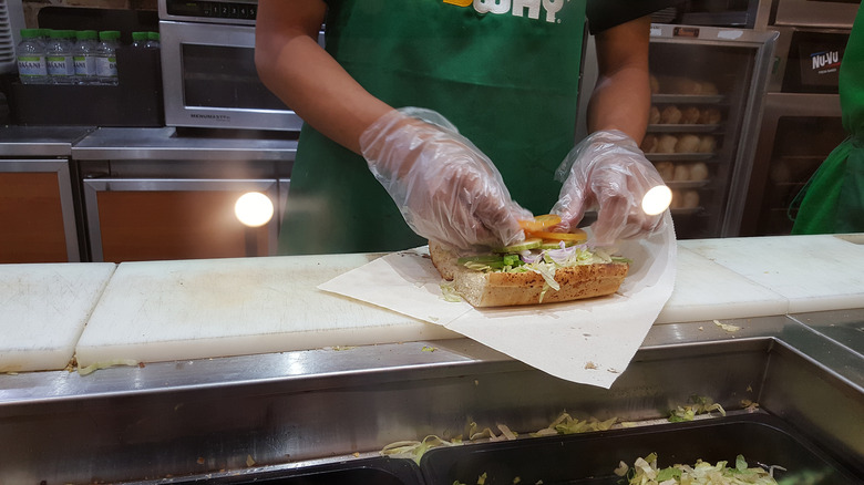 Person in a green apron making a sandwich