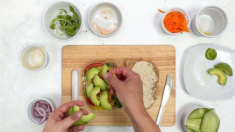 hands putting avocado on sandwich